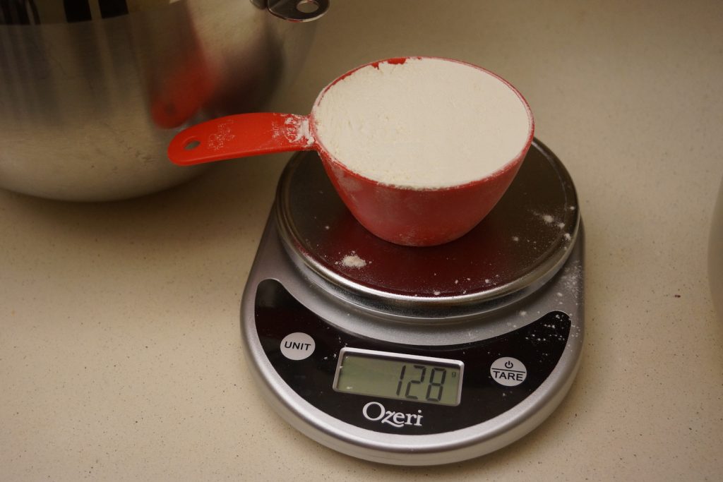 Measuring cup sitting on a kitchen scale, reading 128 grams.